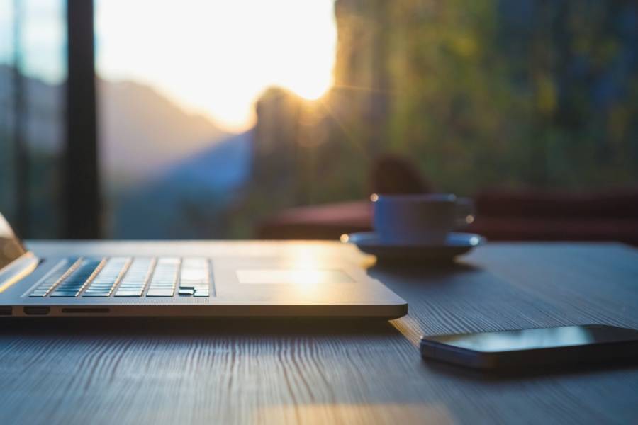 Laptop on a desk with a smartphone and coffee cup, with sunlight streaming through a window—illustrating a calm workspace for getting started.